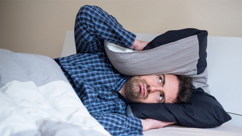 man covering ears in bed